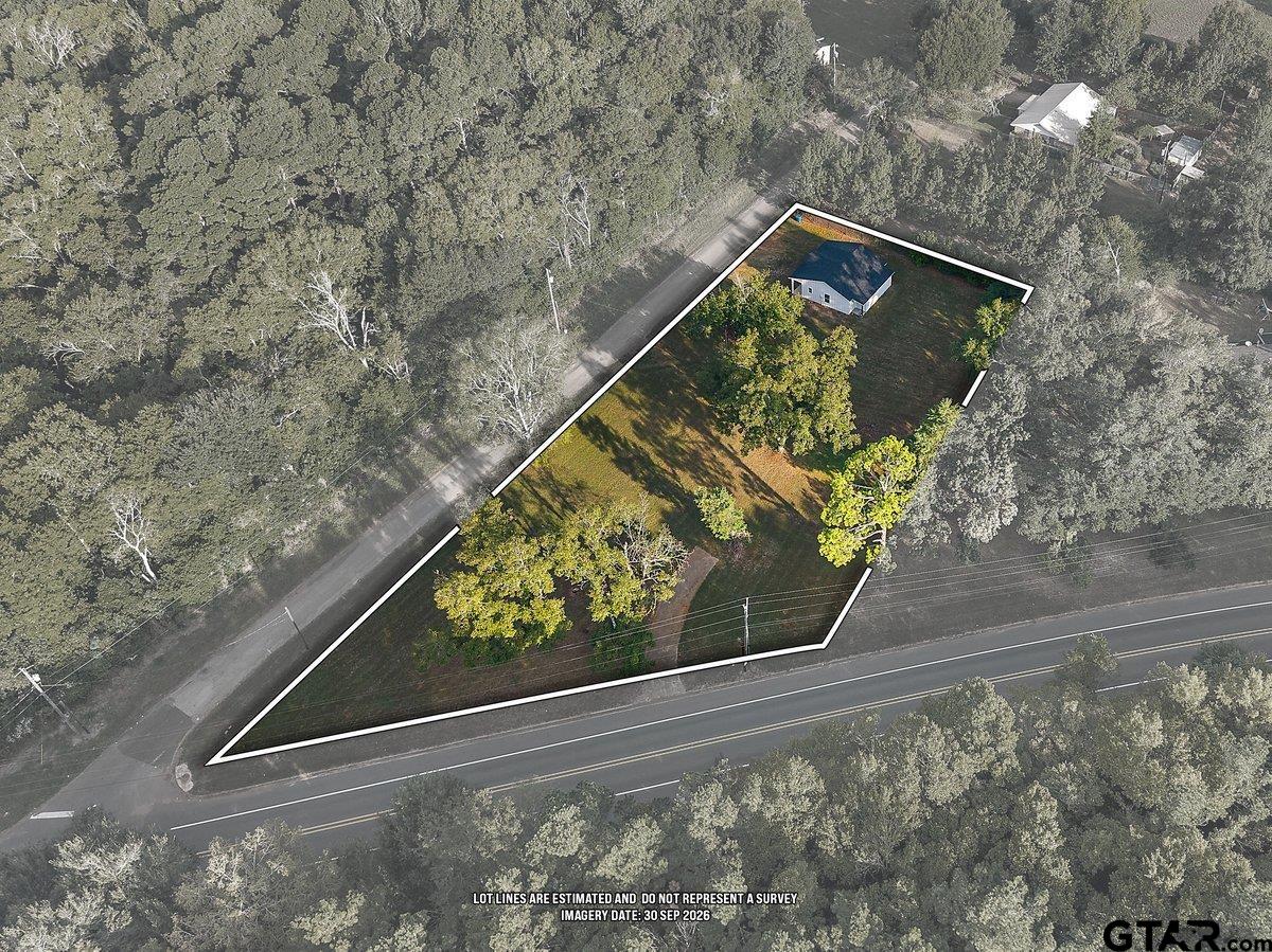 Aerial view of wooded property with a house and estimated lot boundaries along two roads.