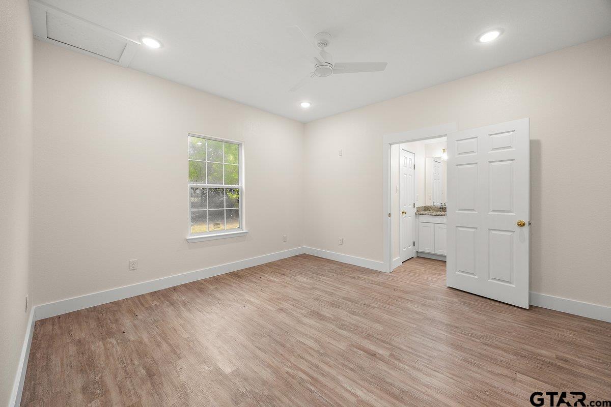 Empty bedroom with wood-look flooring, a ceiling fan, and an open doorway to a vanity area.