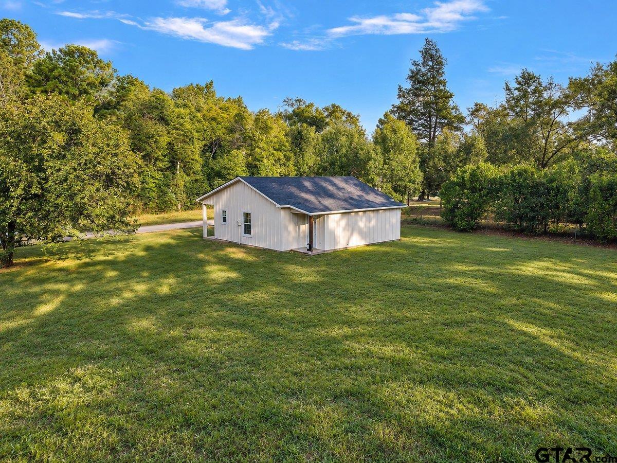 Small white gable-roof building in a grassy clearing surrounded by mature trees.