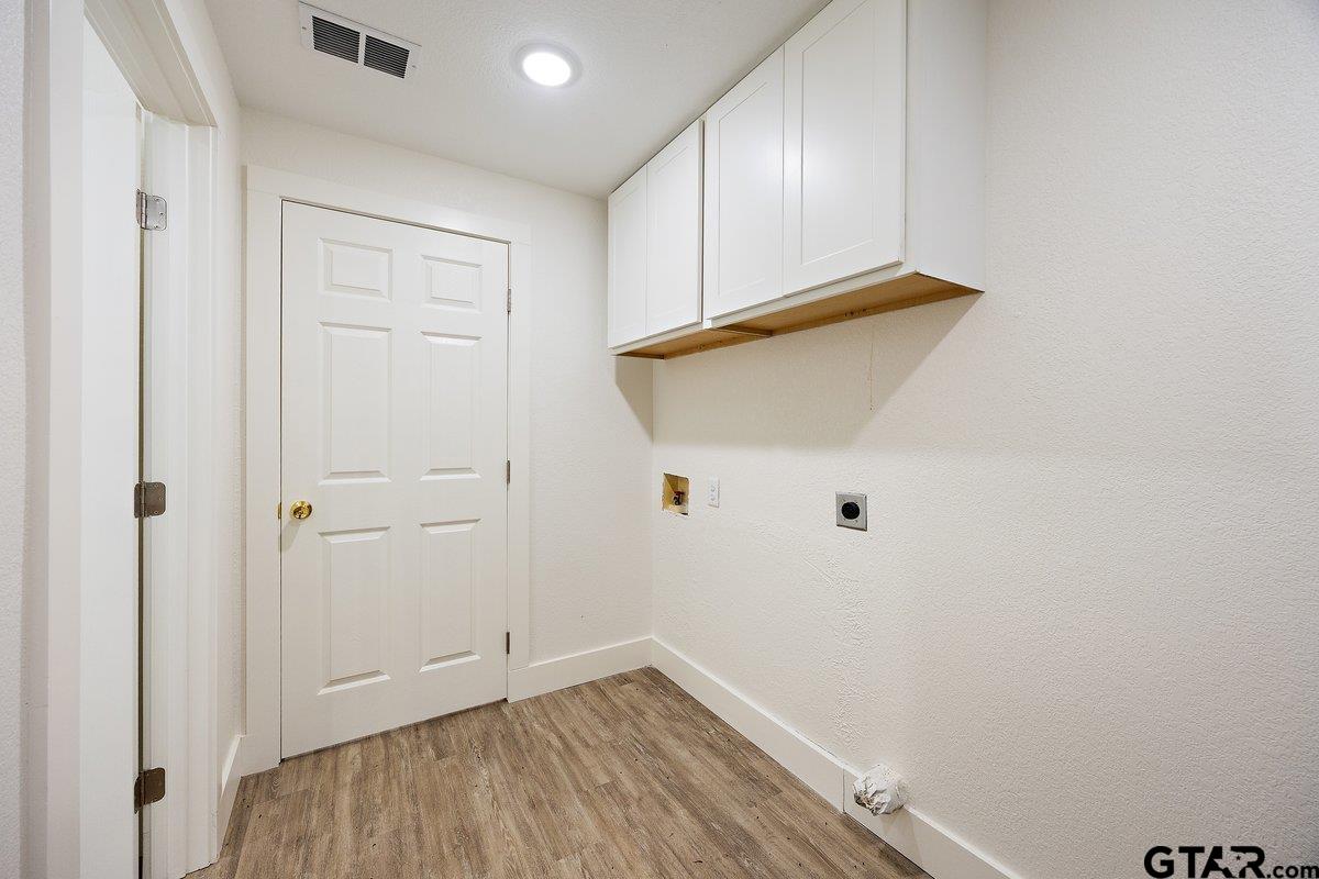 Empty laundry room with white upper cabinets, appliance hookups, and wood-look flooring.