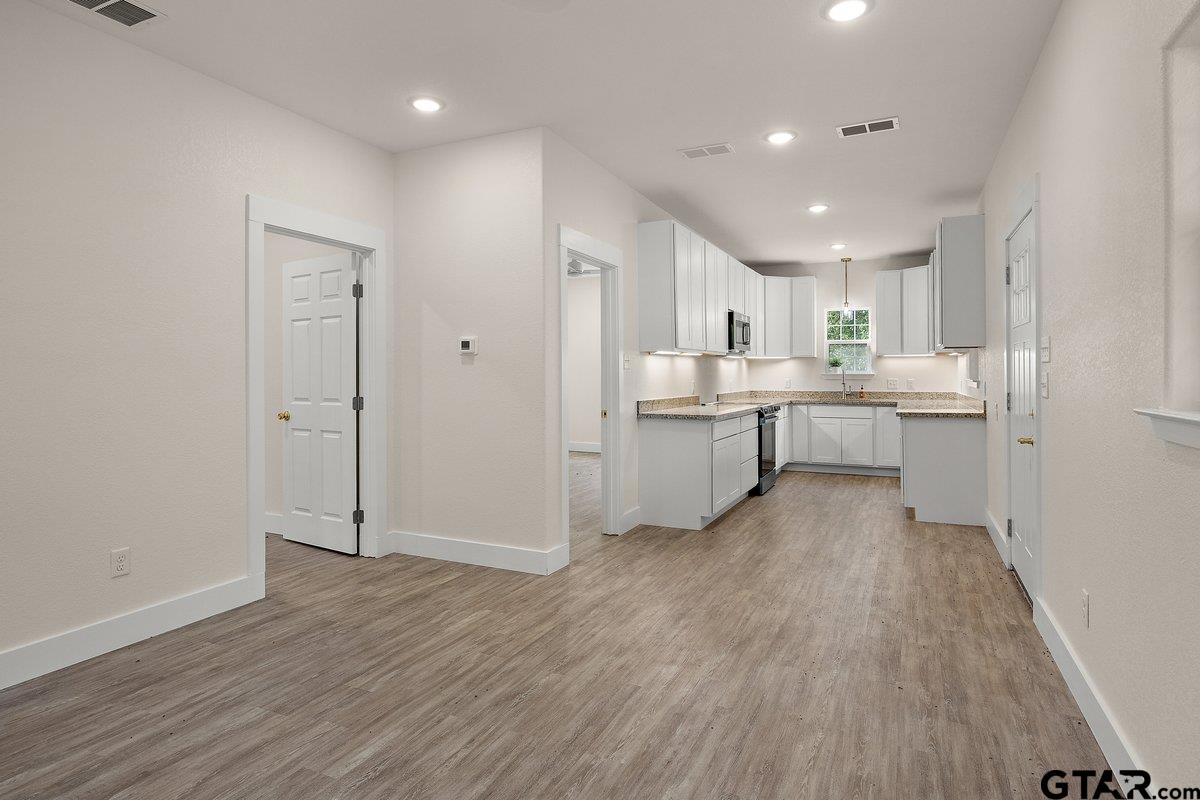 Bright vacant kitchen with white cabinets, granite counters, and wood-look flooring.