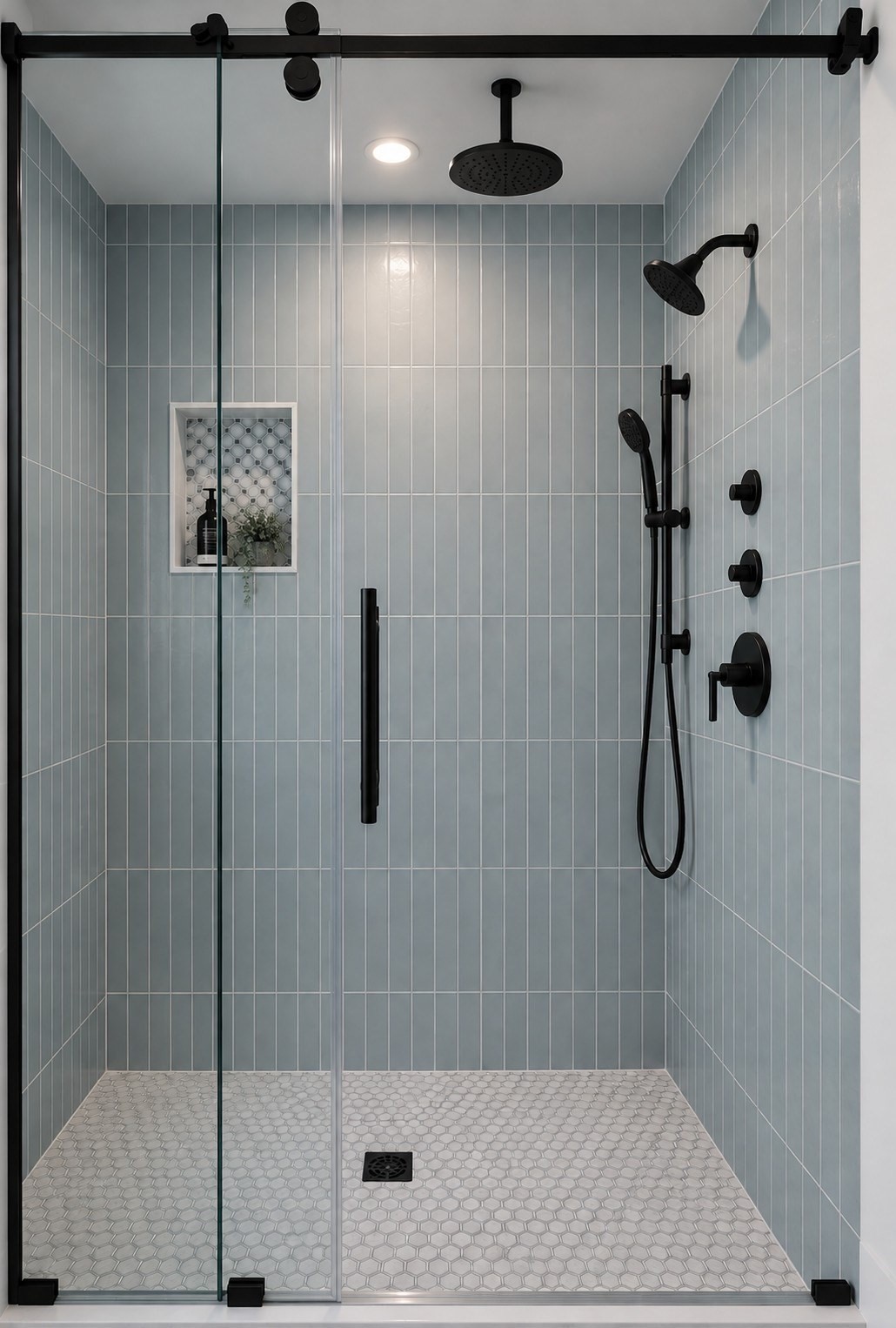 Walk-in shower with blue-gray tile, a glass enclosure, and matte black rain and handheld shower fixtures.