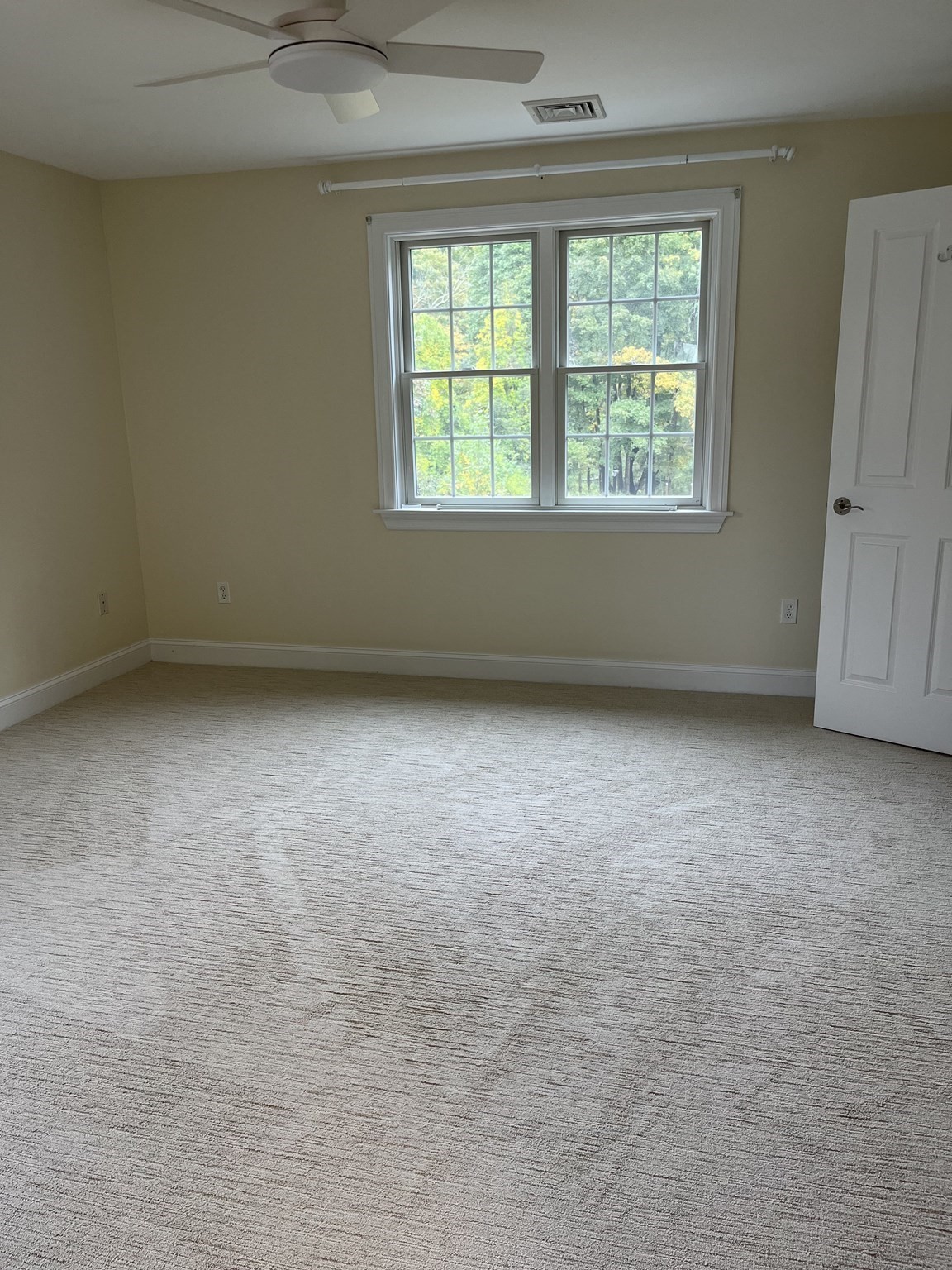 Unfurnished bedroom with a ceiling fan and double window overlooking trees.