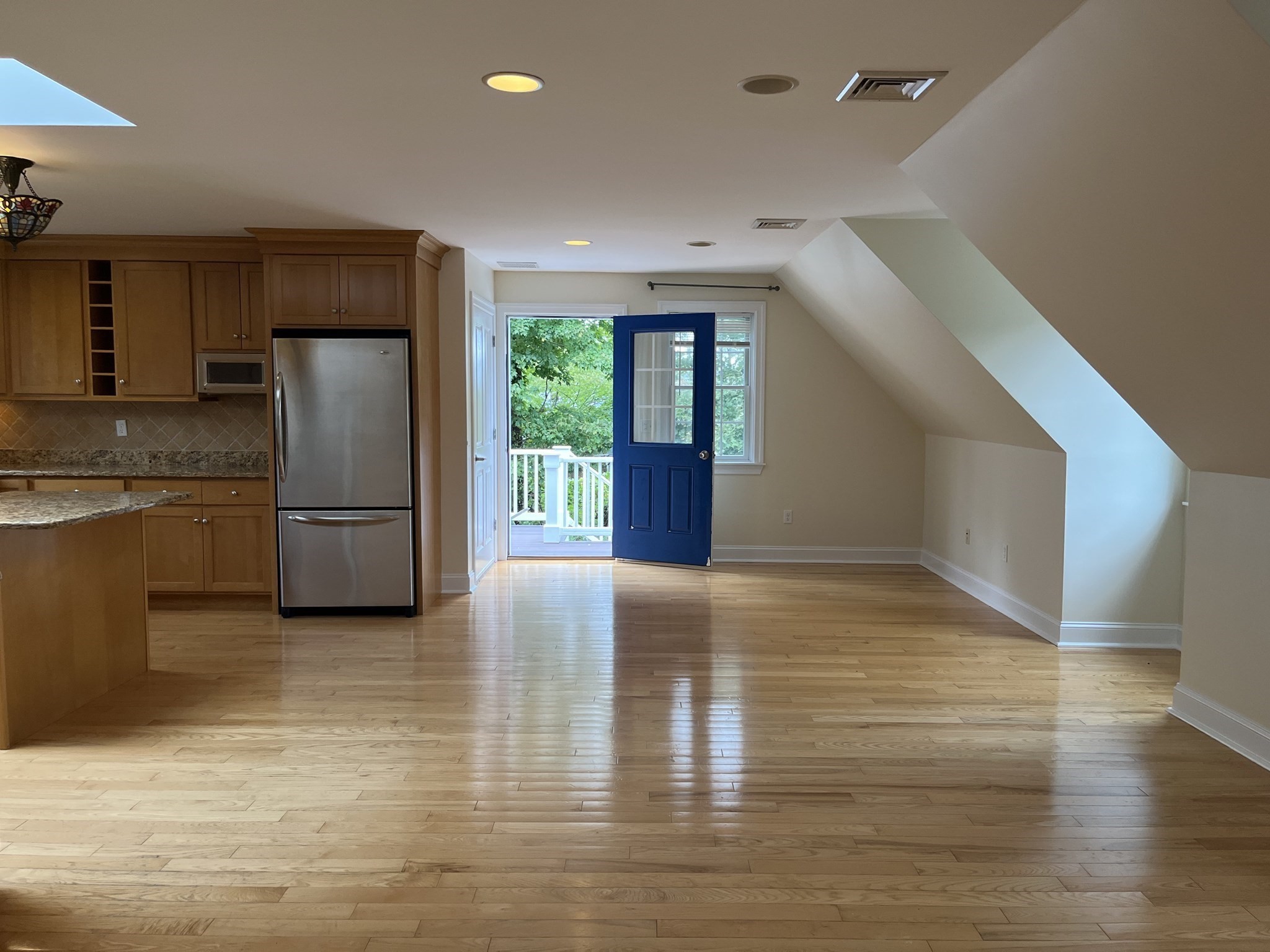 Open kitchen and living area with wood cabinetry, hardwood floors, and a blue door to a balcony.