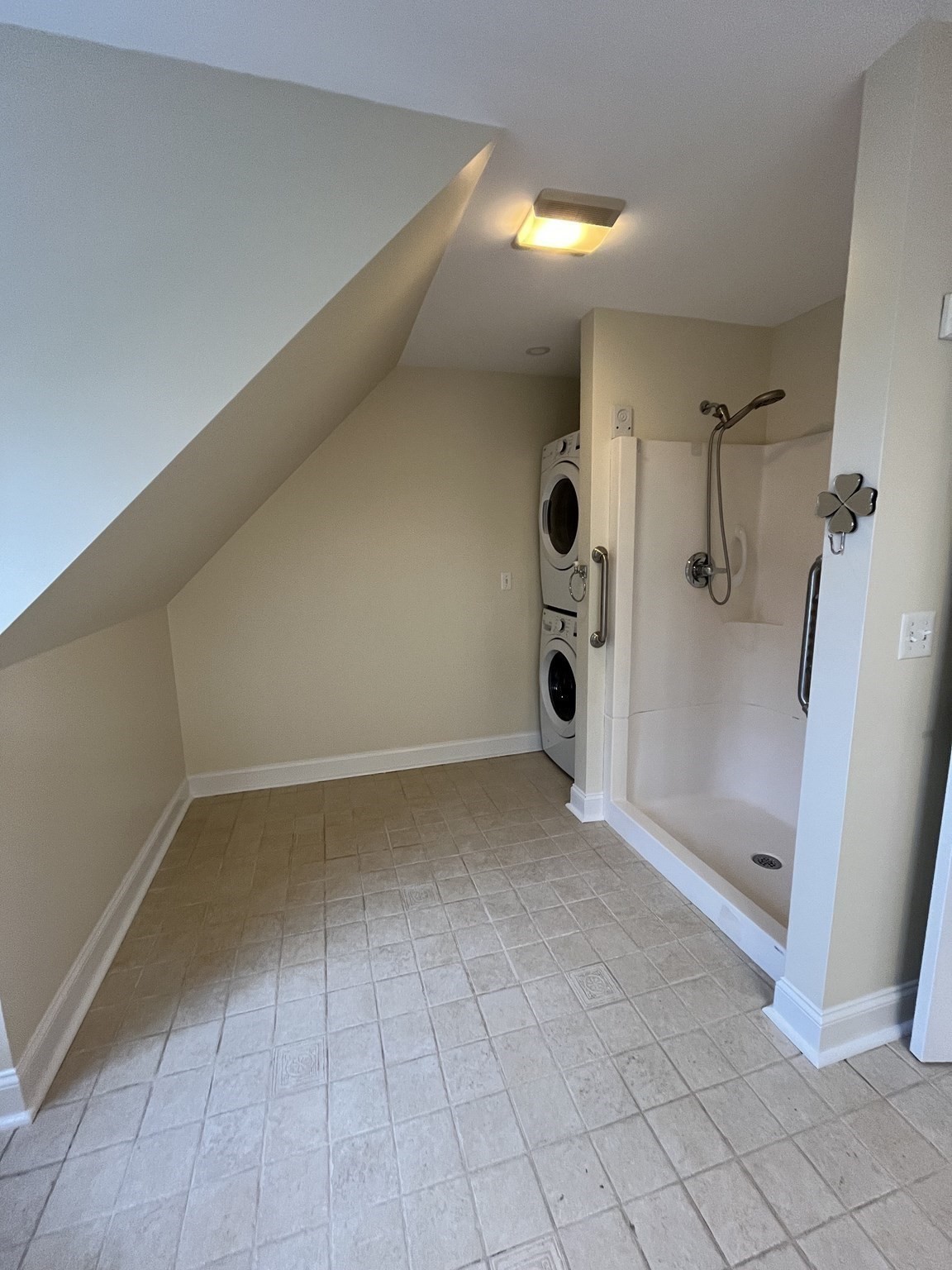 Bathroom with a walk-in shower and stacked washer and dryer beneath a sloped ceiling.