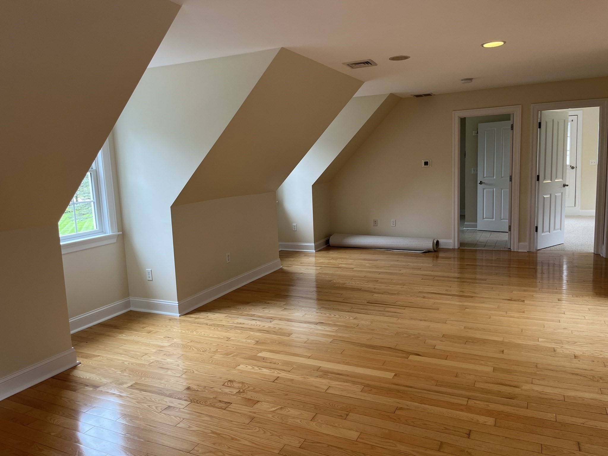 Empty upper-floor room with sloped ceilings, hardwood floors, and a window.