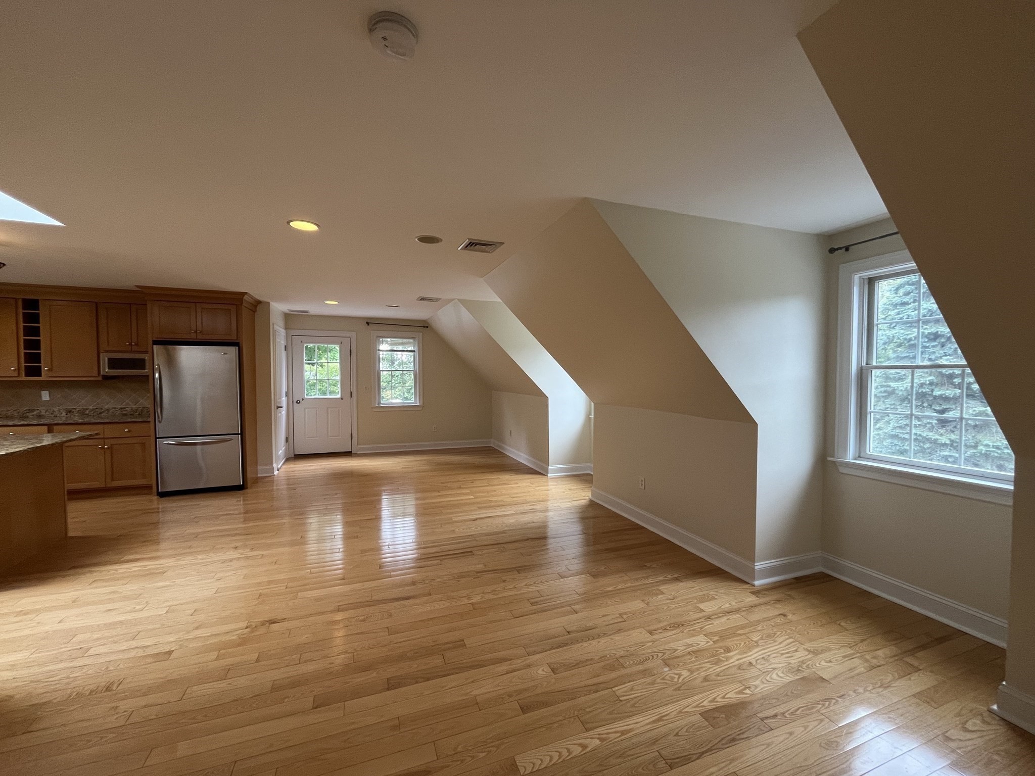 Open living area with hardwood floors, sloped ceilings, and a wood-cabinet kitchen.