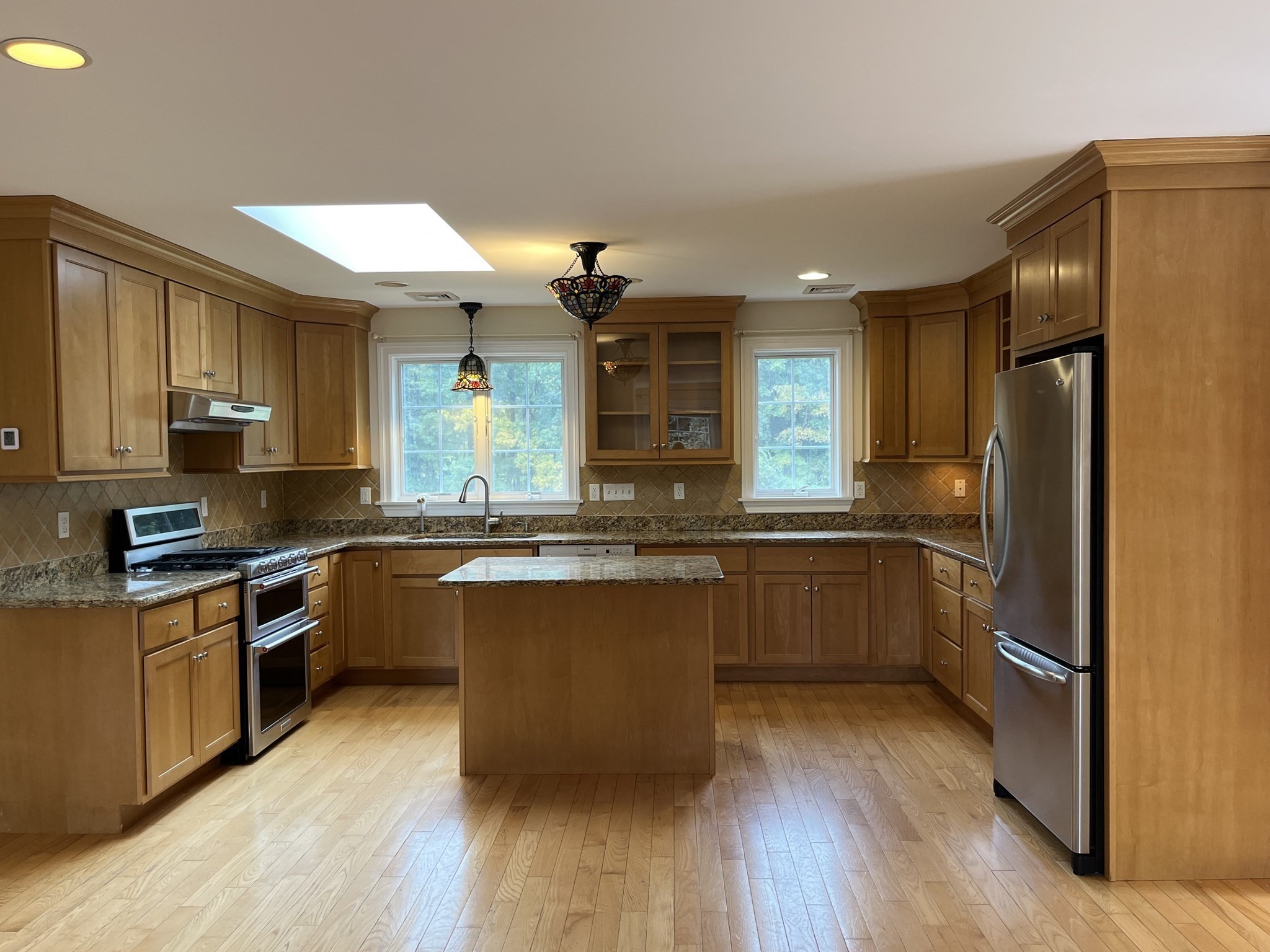 Kitchen with honey-toned cabinets, granite counters, a central island, stainless steel appliances, and a skylight.