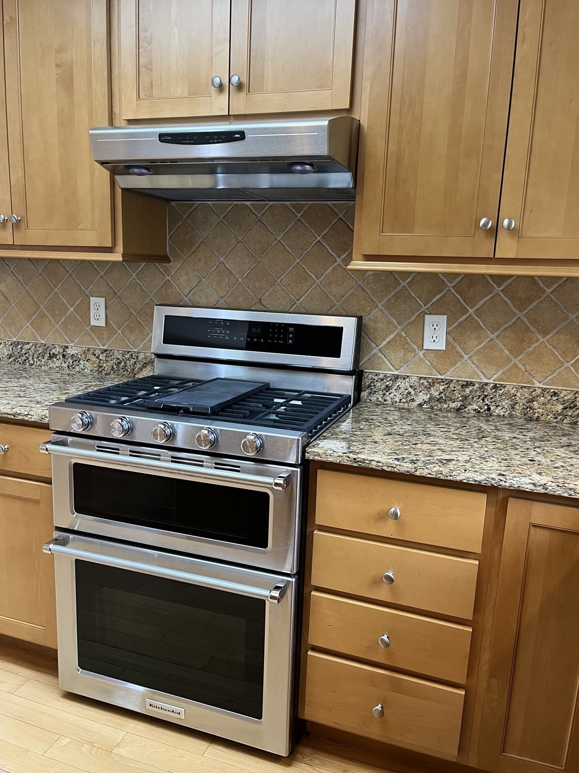 Kitchen range with stainless steel KitchenAid double oven, gas cooktop, wood cabinets, and granite counters.