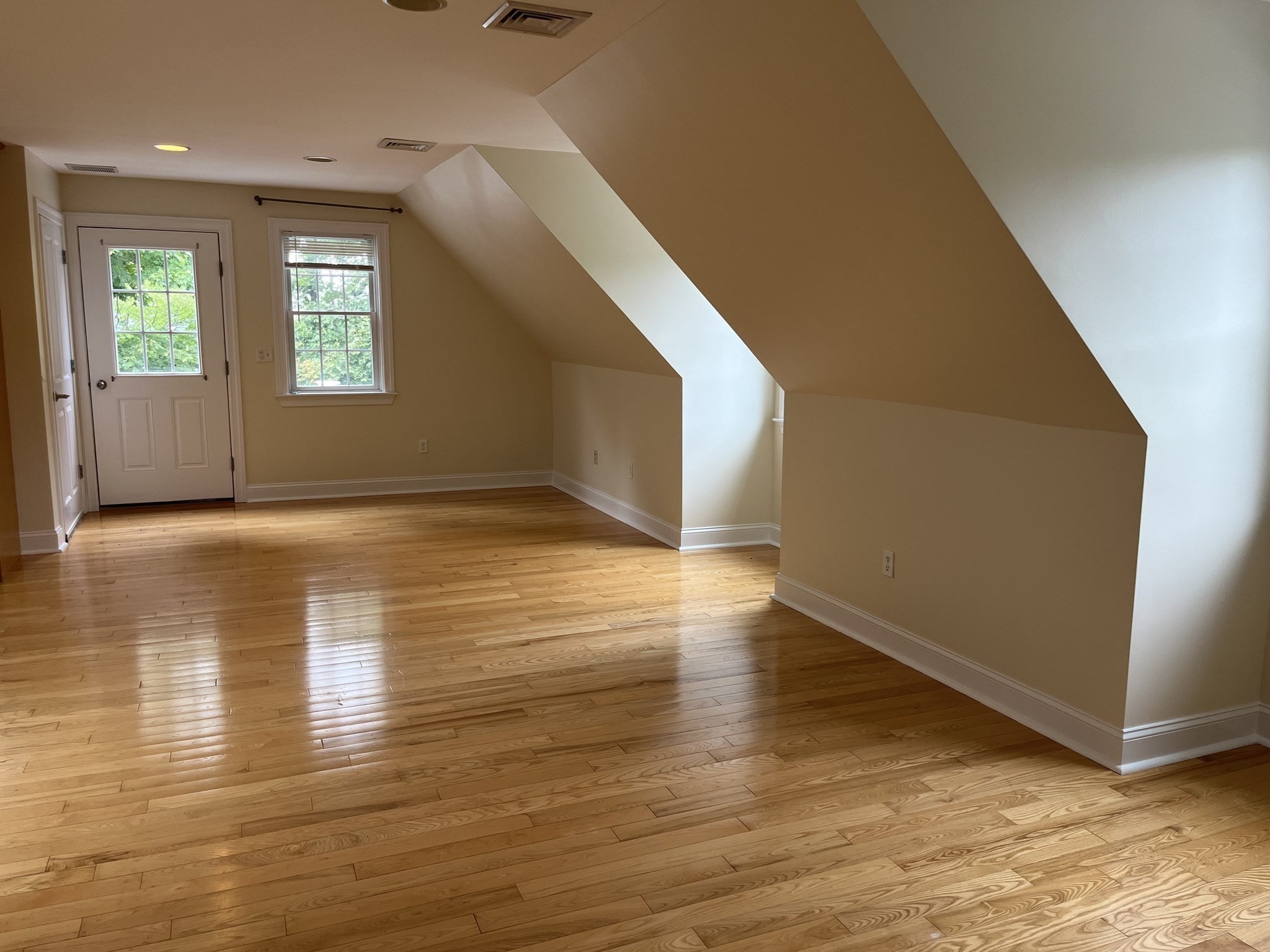 Empty room with polished hardwood floors, a sloped ceiling, and a glazed door beside a window.