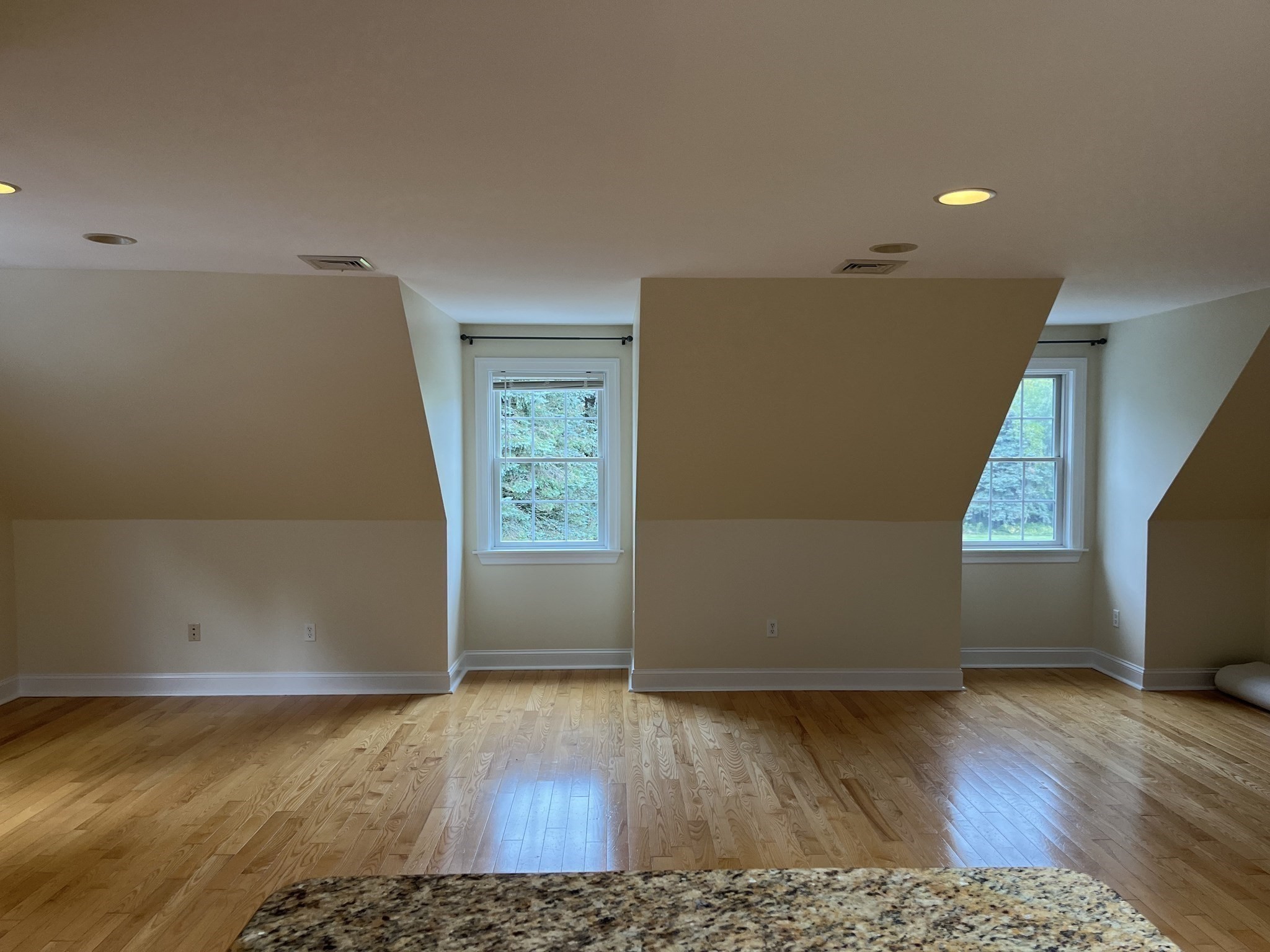 Empty attic room with sloped ceilings, two windows, and hardwood floors.