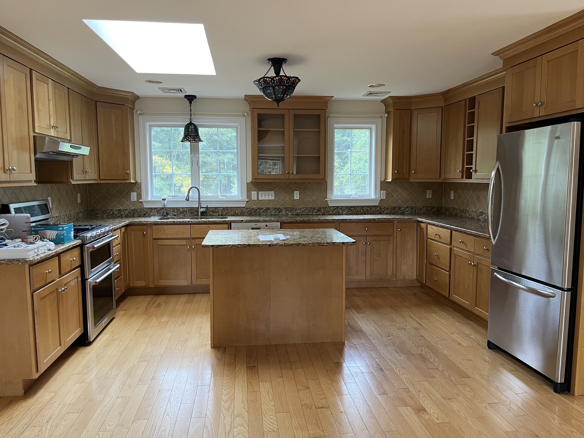 Kitchen with a central island, warm wood cabinetry, granite counters, skylight, and stainless steel appliances.