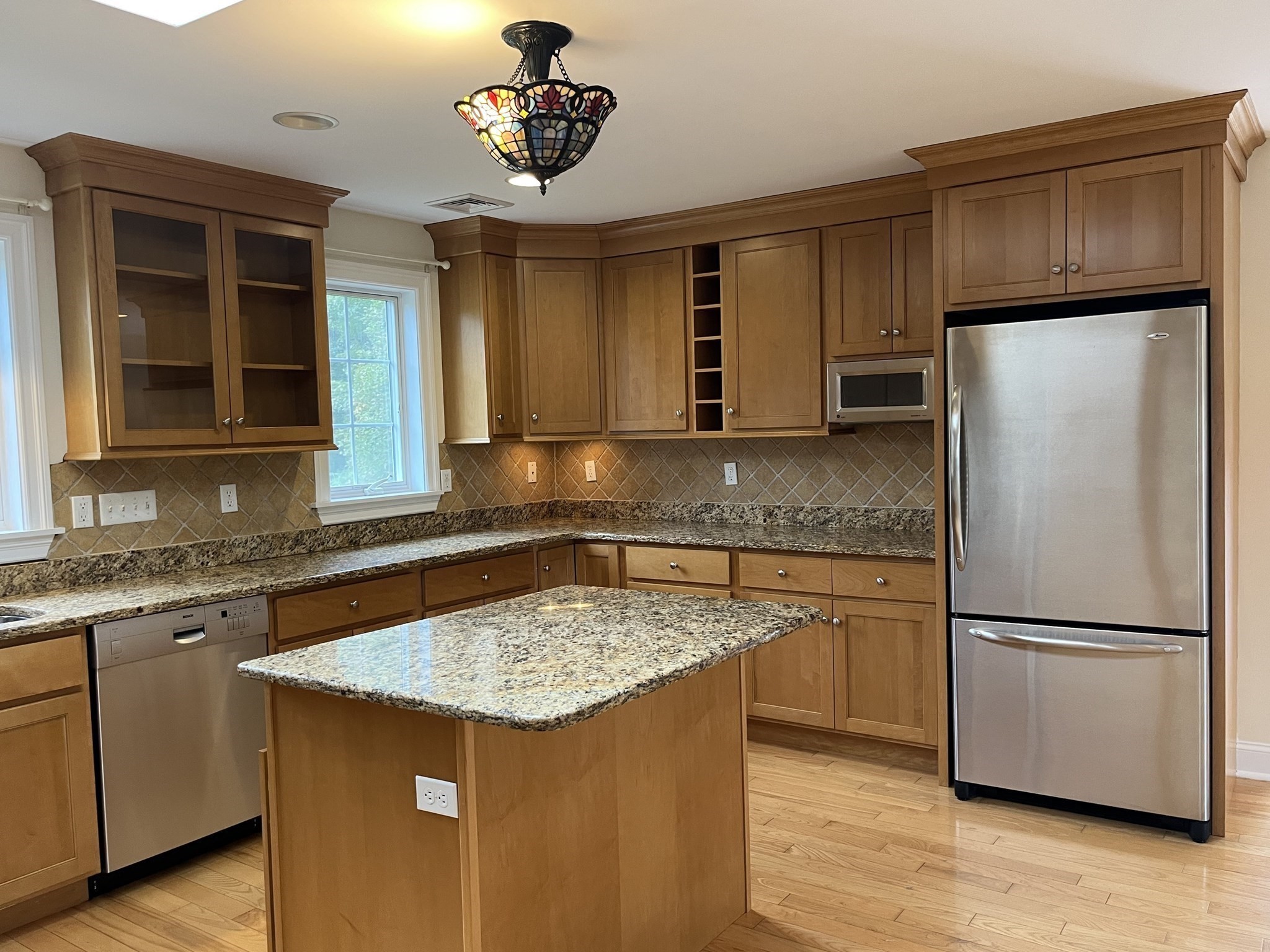 Kitchen with wood cabinets, granite island, stainless steel appliances, and a stained-glass pendant light.
