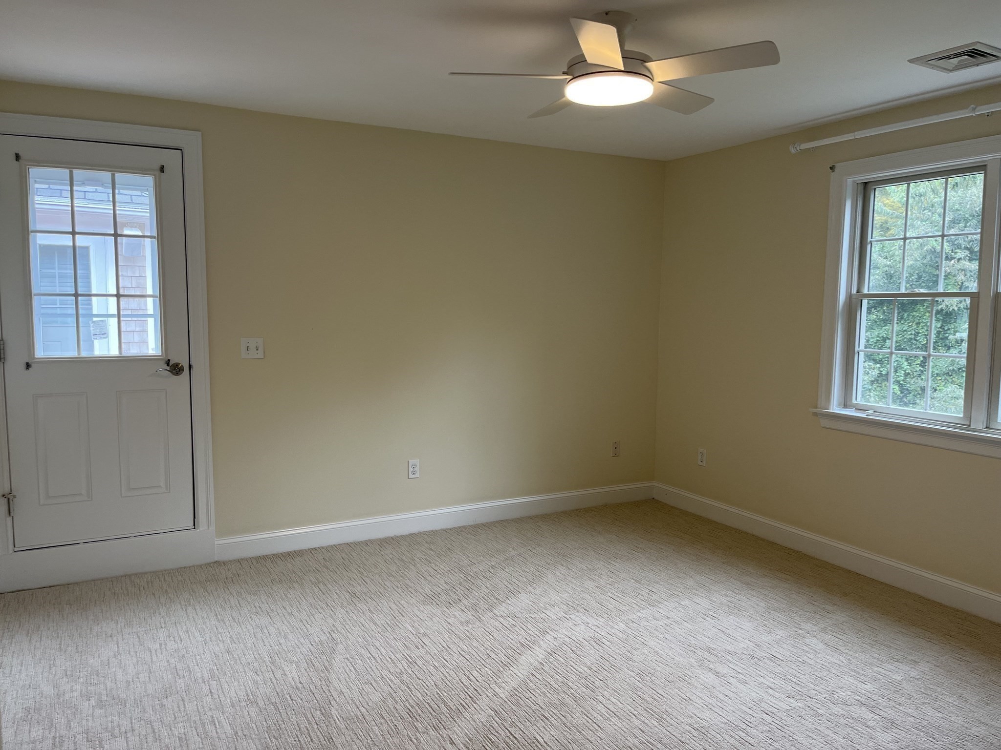 Empty carpeted room with beige walls, a ceiling fan, and two windows.