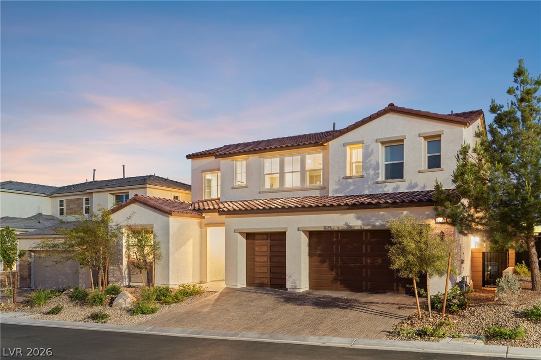 Two-story stucco house with a red tile roof, double garage, and desert landscaping at golden hour.
