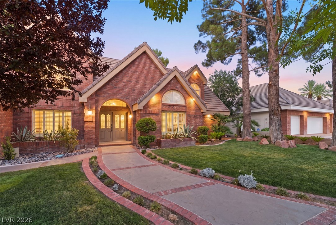 Brick home with an illuminated arched entry, landscaped lawn, and curved driveway at dusk.