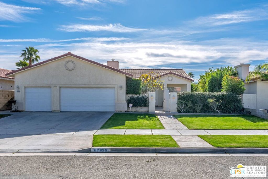 Single-story stucco home with a two-car garage, gated entry, and green lawn.