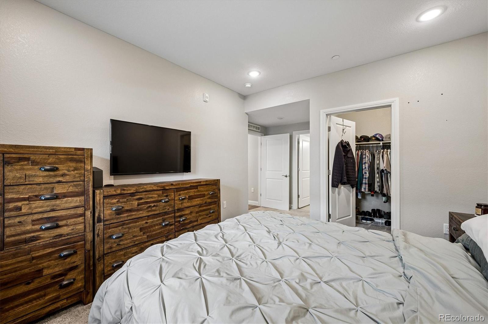 Bedroom with a white tufted bed, rustic wood dressers, wall-mounted television, and open clothes closet.