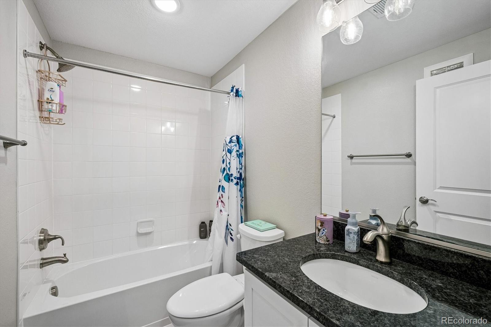 Bathroom with a white tub, patterned shower curtain, and dark granite vanity counter.
