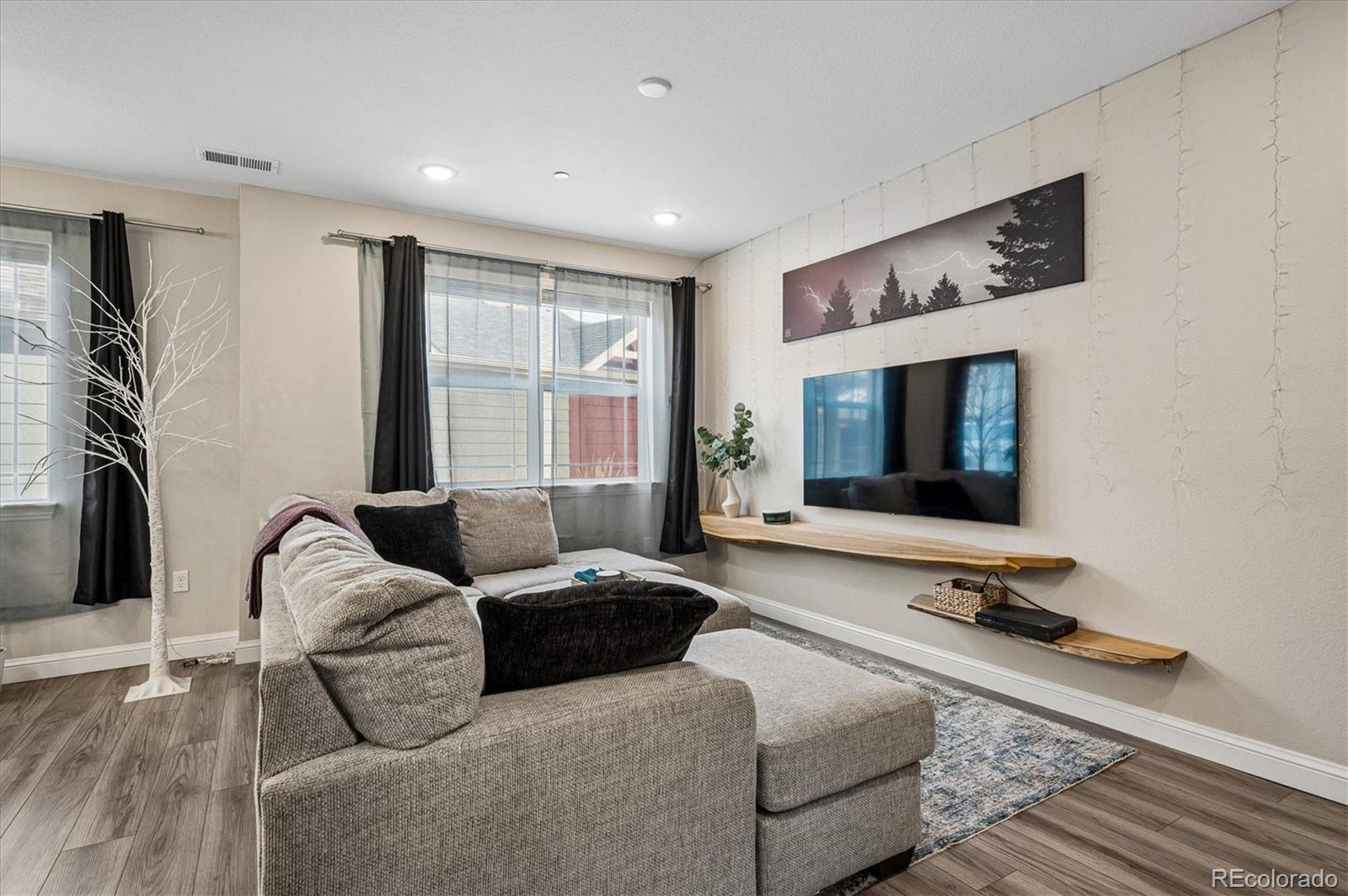 Living room with a gray sectional, wall-mounted TV, floating shelves, and dark curtains.