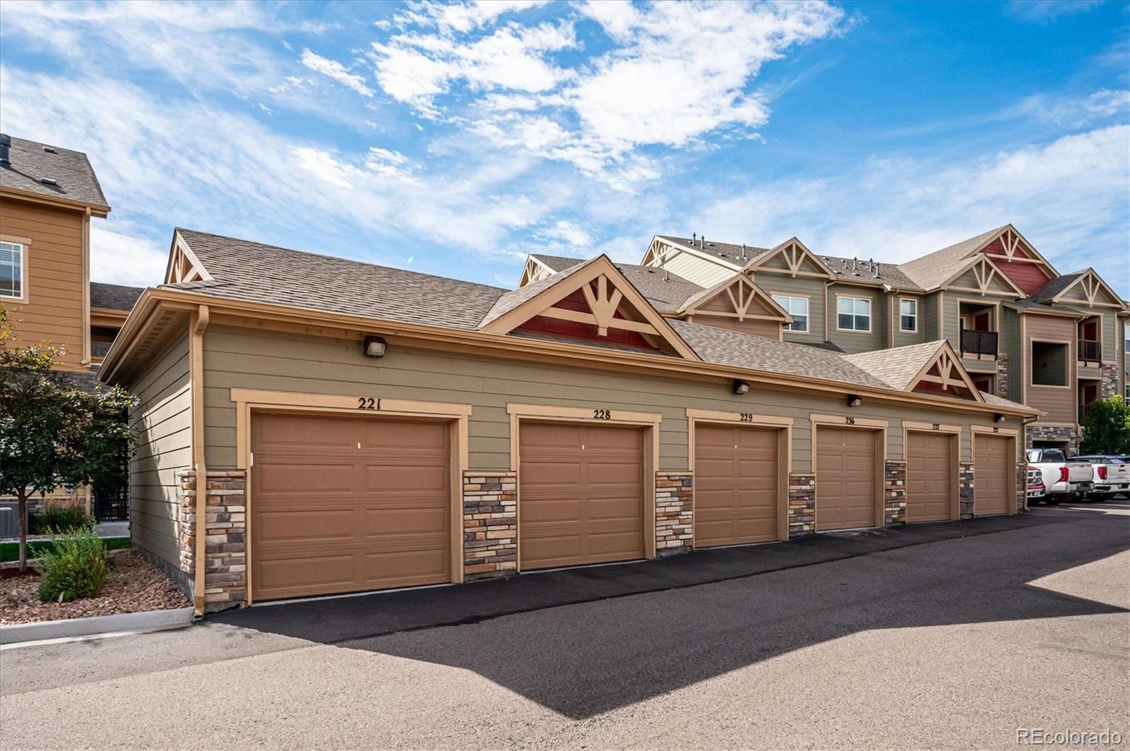 Row of tan condominium garages with numbered doors and multi-unit buildings behind them.