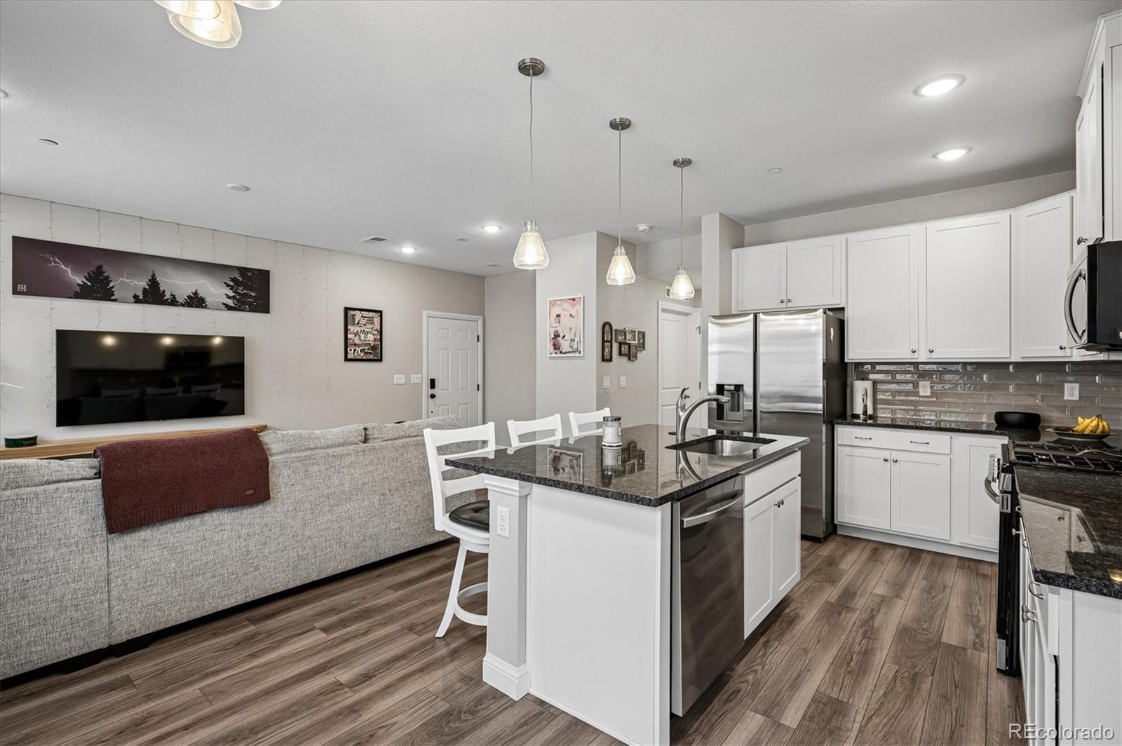 Open-plan kitchen and living area with a dark stone island, white cabinetry, and stainless steel appliances.