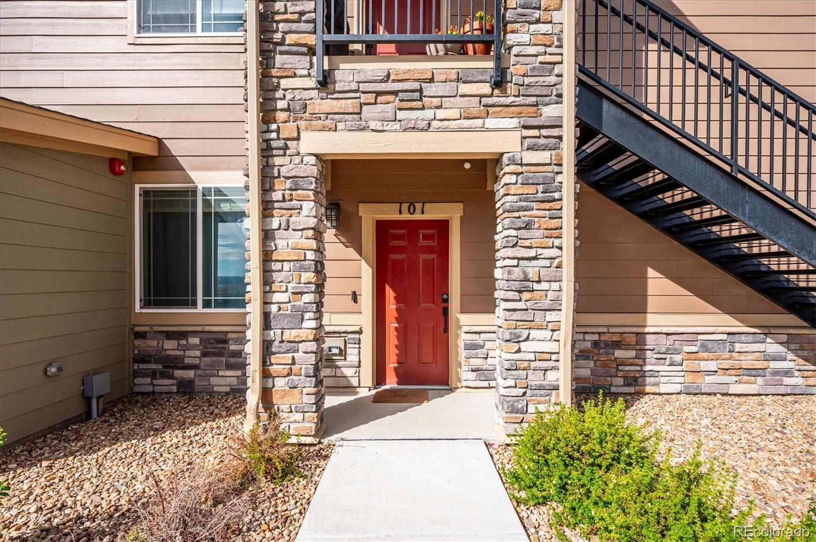 Condo entrance with a red door marked 101, stone columns, and an exterior staircase.