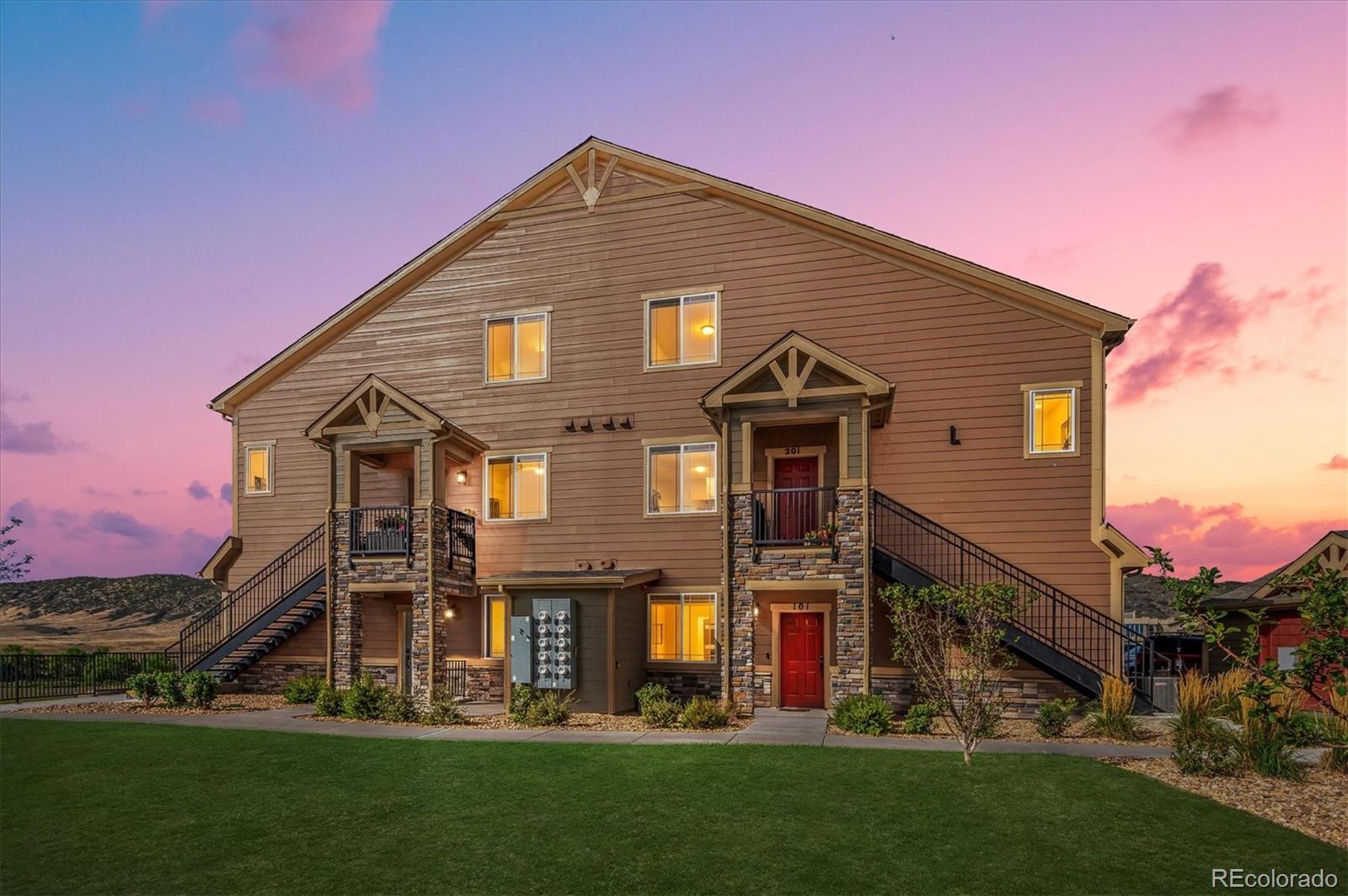 Multi-unit building with stone entry columns and exterior staircases beneath a pink dusk sky.