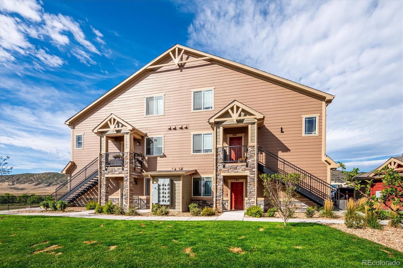 Tan condominium building with stone accents, red doors, balconies, and exterior staircases.