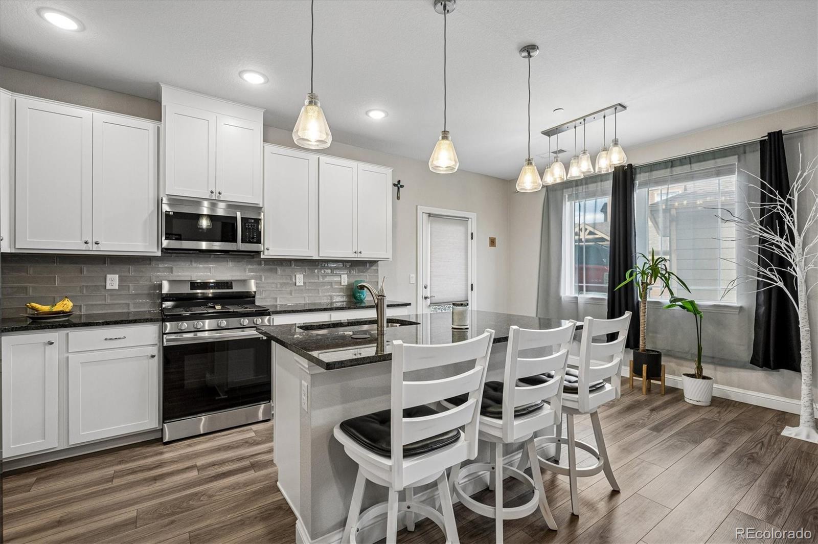 Kitchen with white cabinets, stainless steel appliances, a large island, and white bar stools.