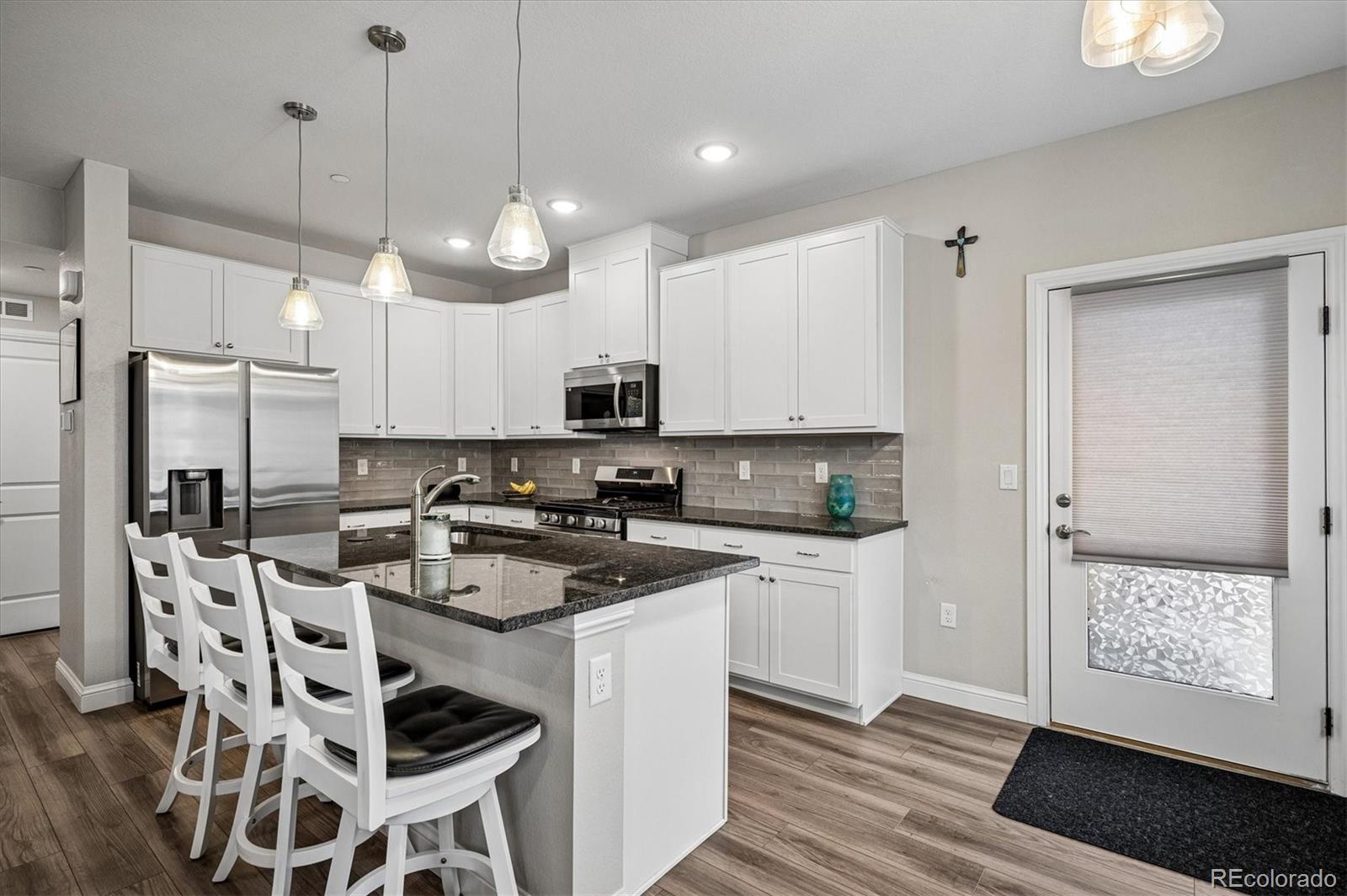 Kitchen with white cabinets, stainless steel appliances, and a granite island with bar seating.