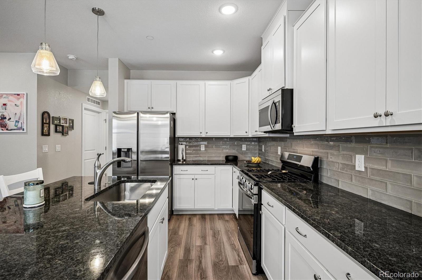 Kitchen with white cabinets, dark granite counters, gray tile backsplash, and stainless steel appliances.