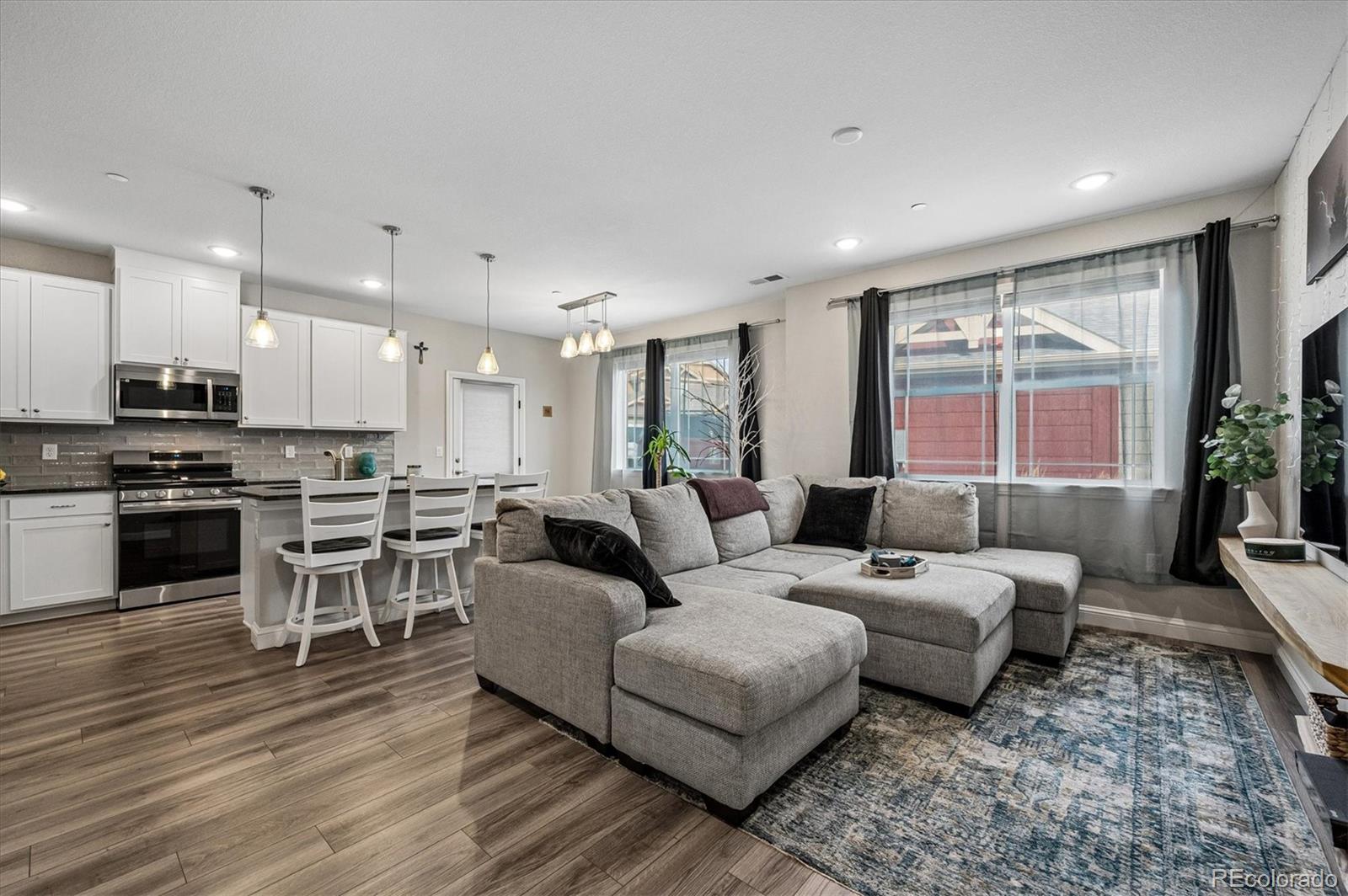 Open-plan living room and kitchen with a gray sectional, white cabinetry, and large windows.