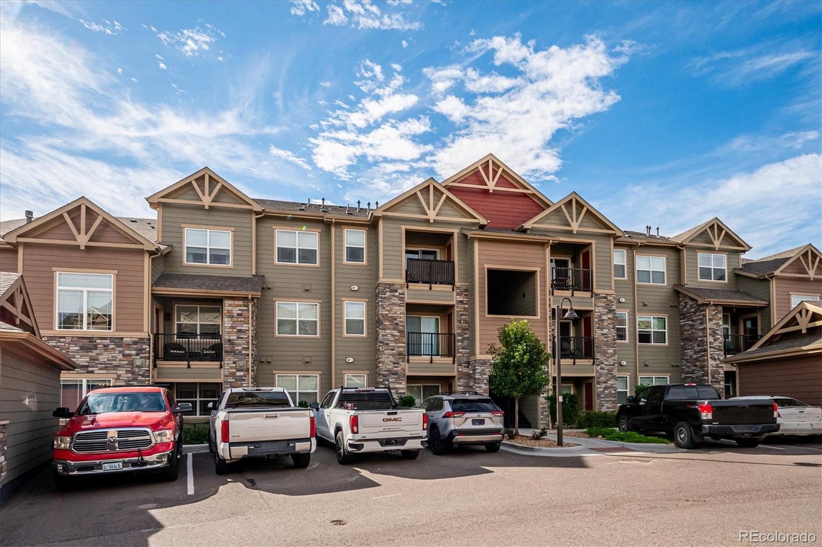 Multi-story condominium exterior with balconies, stone accents, and parked vehicles.