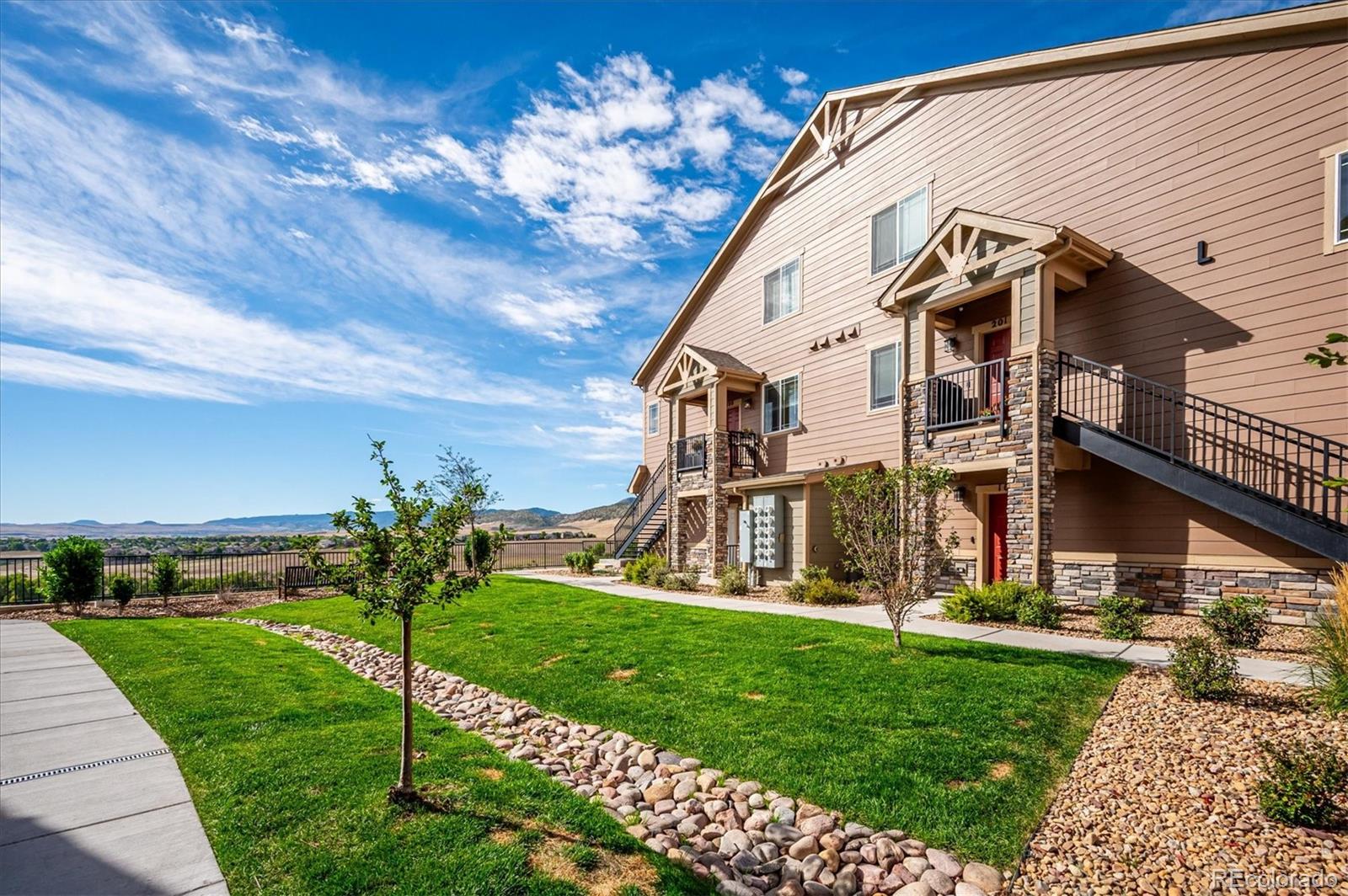 Multi-unit residence with stone-accented balconies beside a landscaped lawn and distant foothills.
