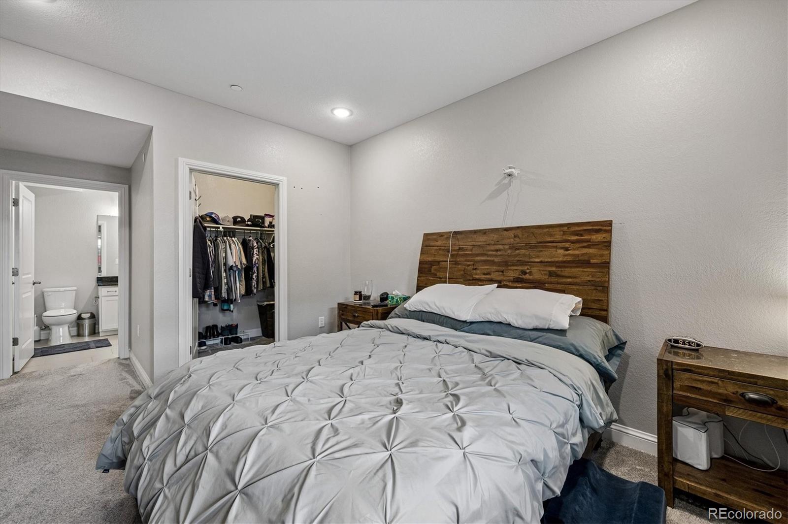 Bedroom with a gray duvet, rustic wood headboard, open clothes closet, and adjoining bathroom doorway.