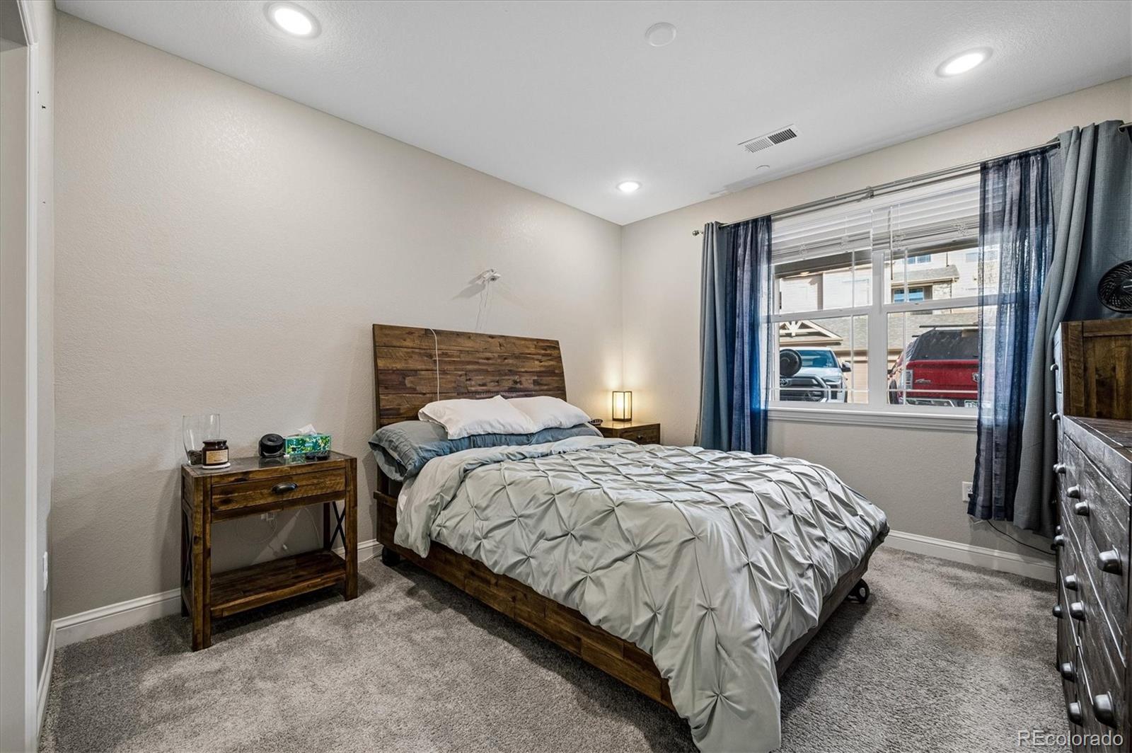 Furnished bedroom with a rustic wooden bed, gray patterned bedding, and blue curtains.