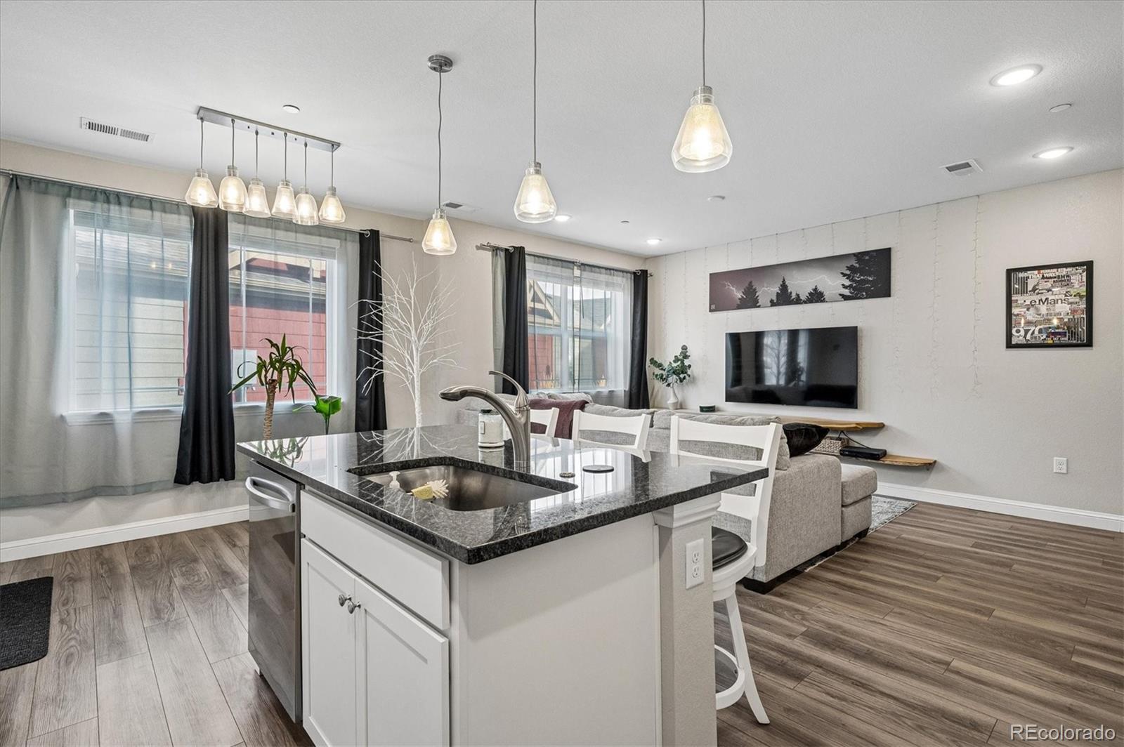 Open-plan kitchen and living room with a granite island, pendant lights, and gray sofa.