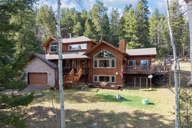 Wood-sided mountain home with a stone garage and elevated decks, surrounded by mature trees.