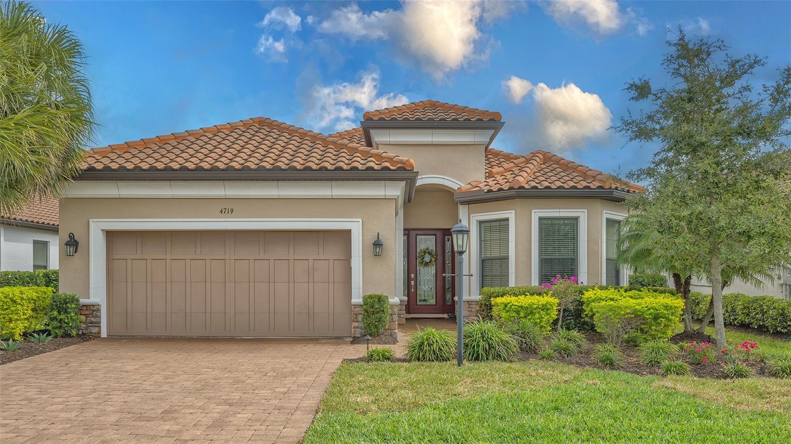 Beige home with a terracotta tile roof, two-car garage, and landscaped front yard.