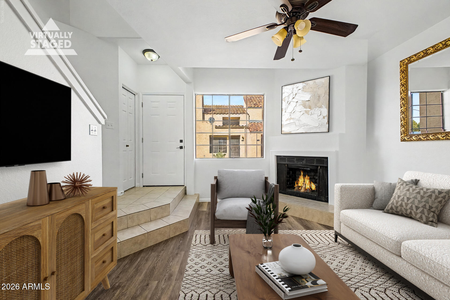 Virtually staged living room with a fireplace, white sofa, patterned rug, and tiled entry steps.
