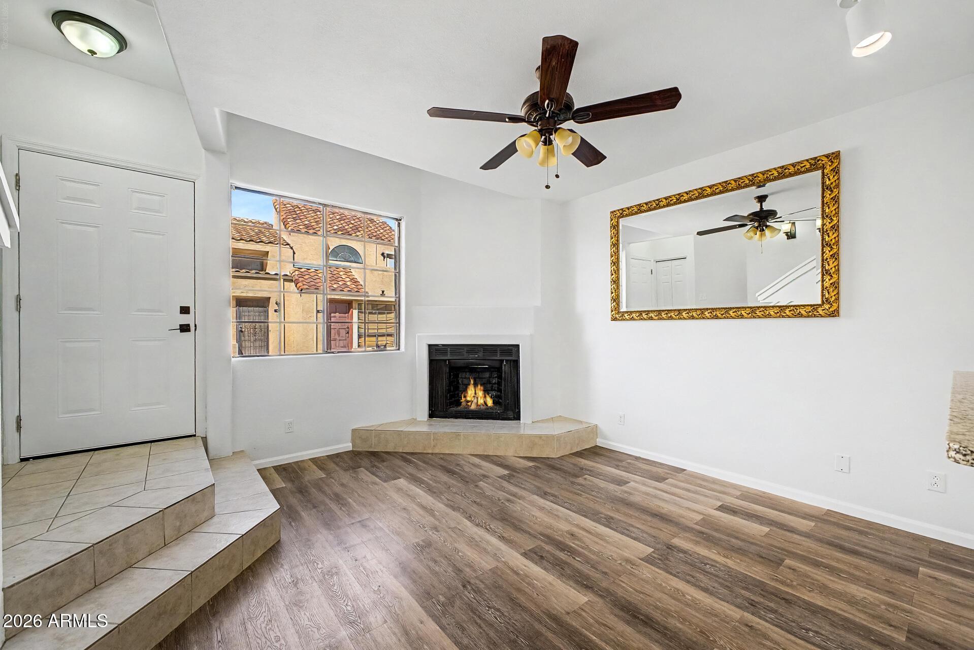 Unfurnished living room with a corner fireplace, large window, and ornate gold-framed mirror.
