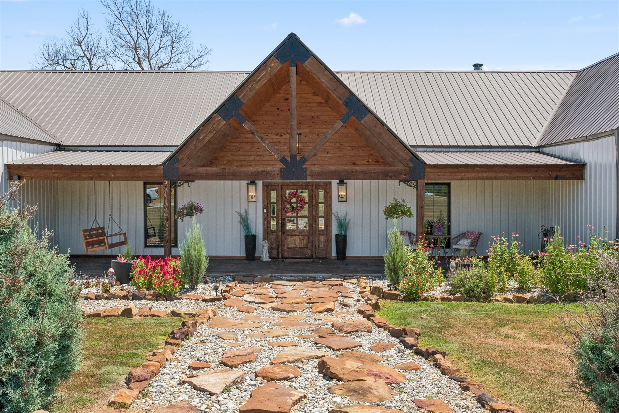 Home exterior with a timber gable porch and stone path through colorful flower beds.