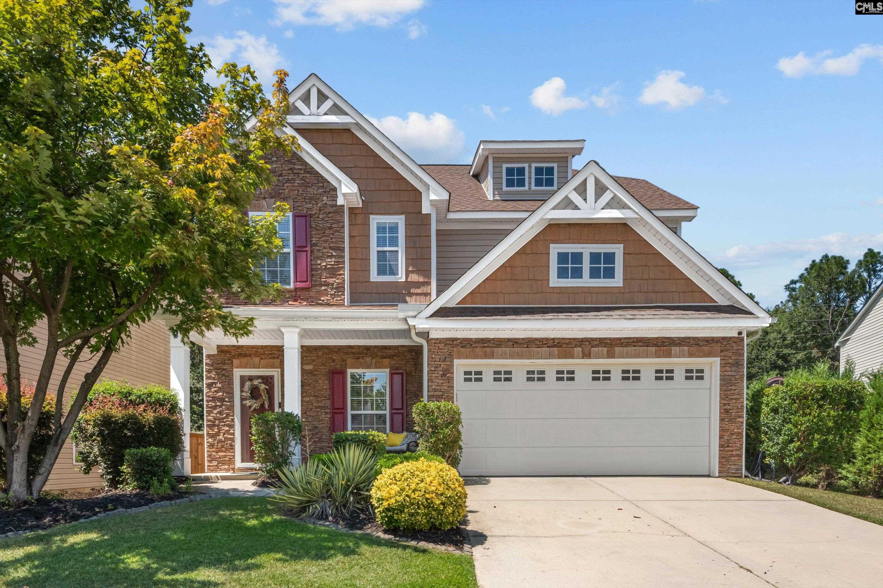 Two-story brown house with stone accents, white-trimmed gables, and a two-car garage.