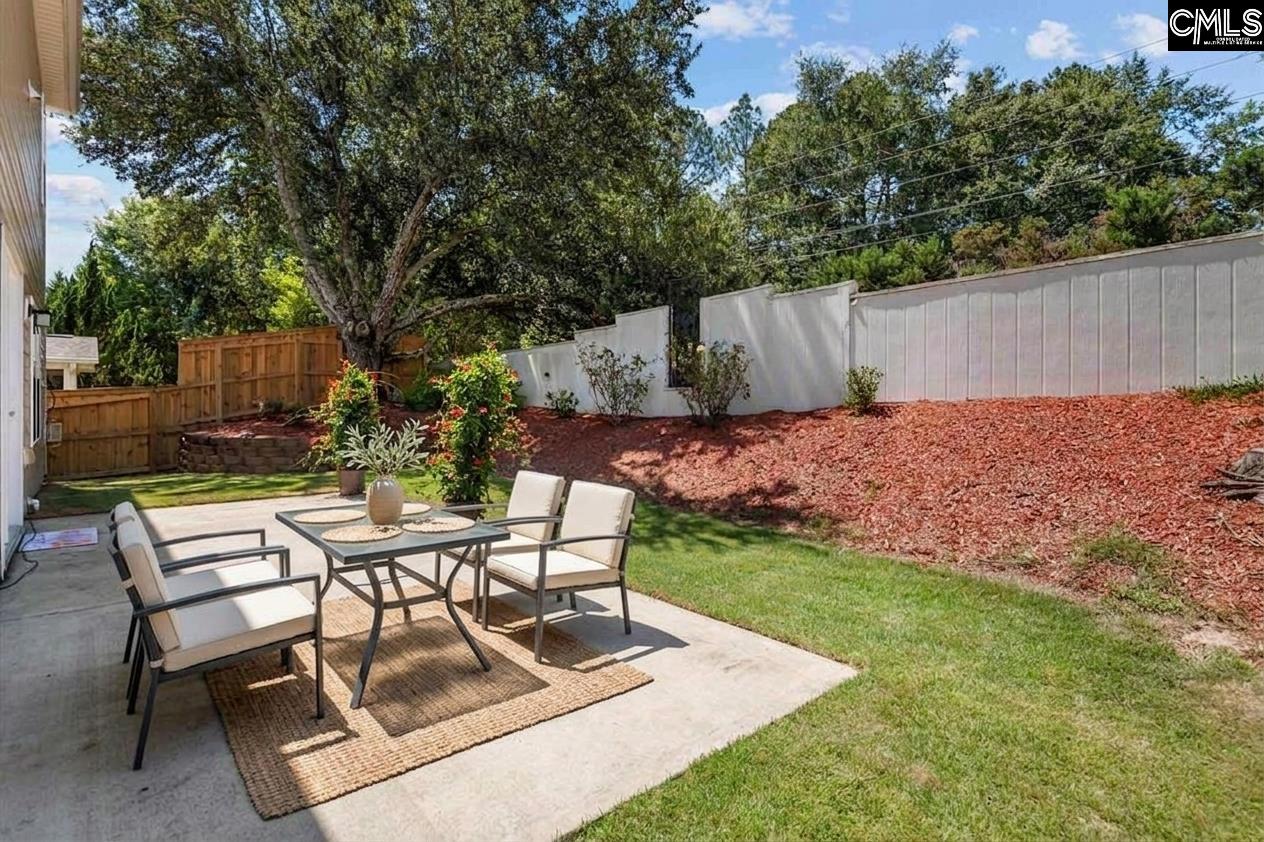 Backyard patio with outdoor dining set, lawn, landscaped slope, privacy fence, and mature trees.