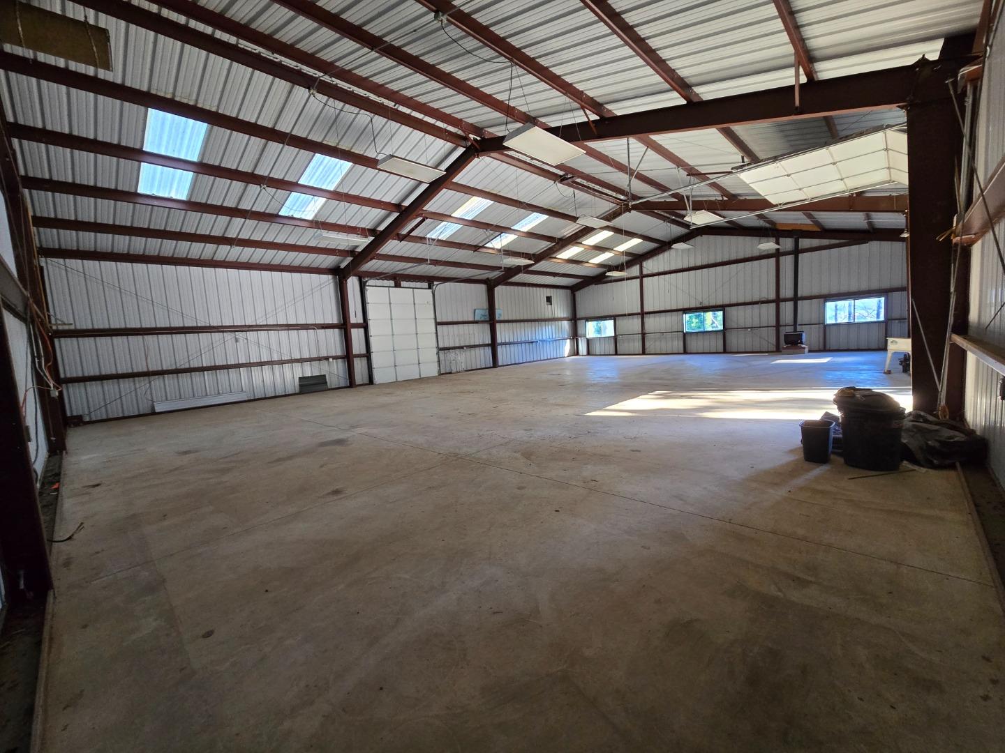 Vacant barn interior with a concrete floor, exposed steel trusses, skylights, and overhead door.