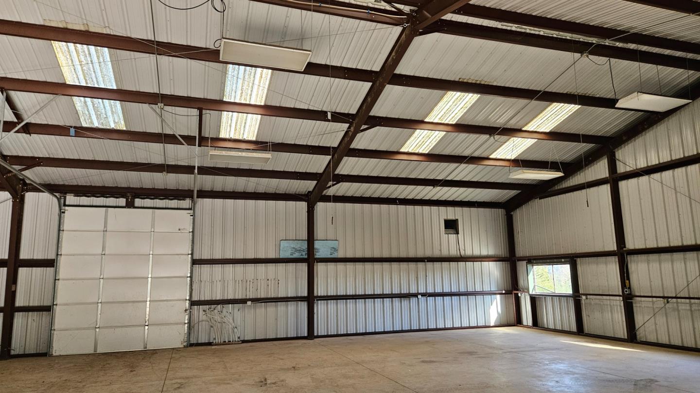 Vacant metal outbuilding with exposed steel beams, skylights, and a large sectional garage door.
