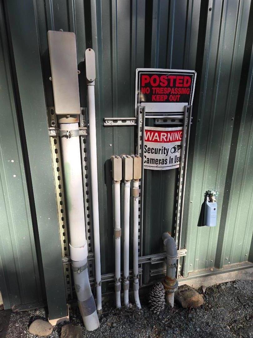 Utility pipes and no-trespassing security signs mounted on green metal siding.