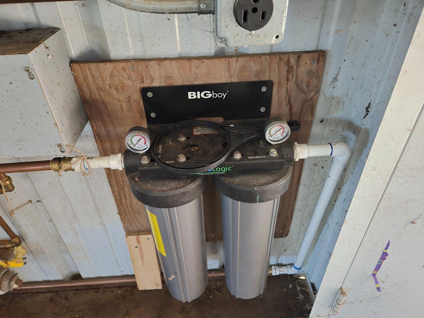 Dual-canister water filtration system with pressure gauges and connected plumbing.