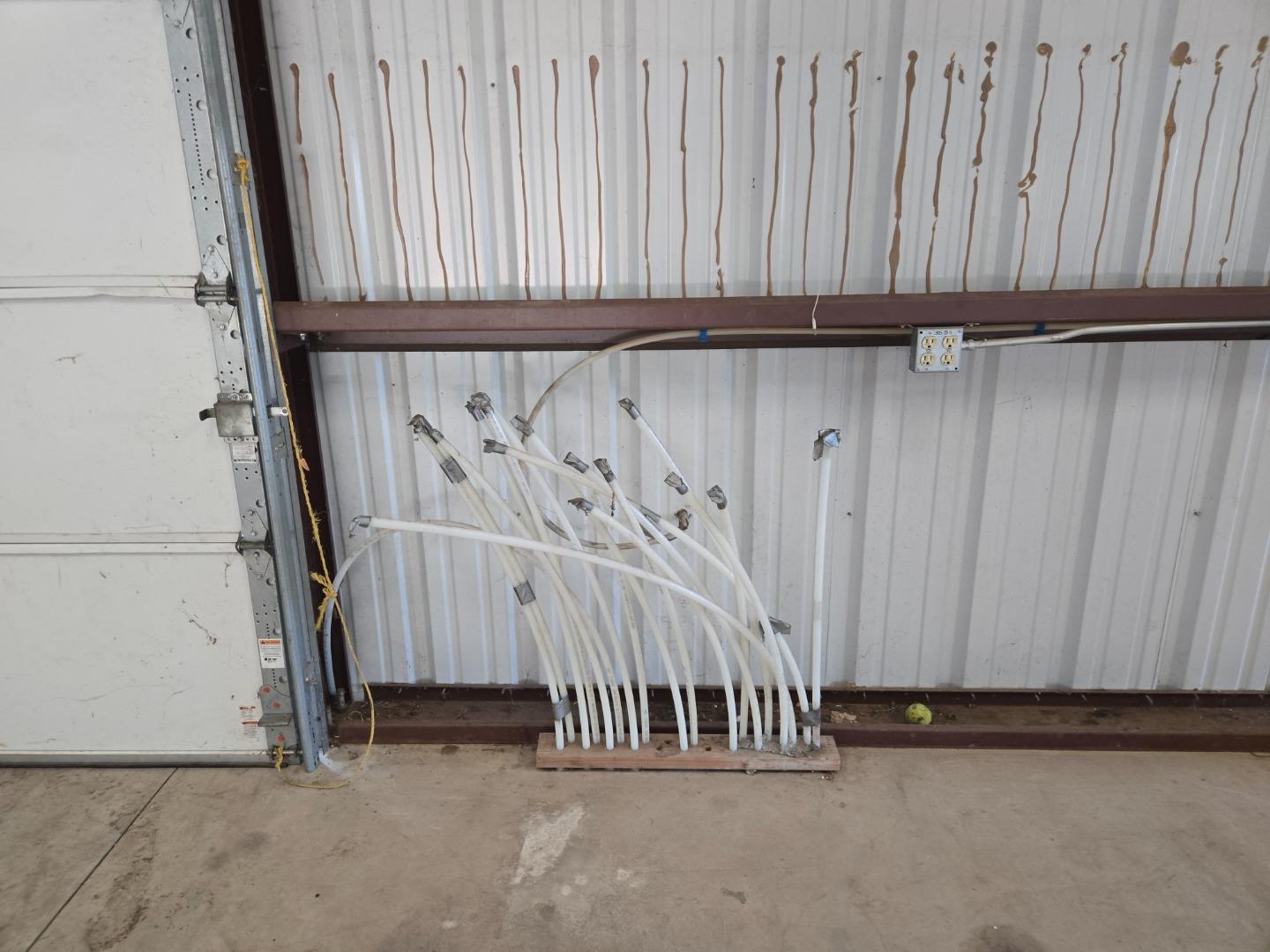 Garage wall with brown streaks, exposed outlet, and white pipes gathered along the concrete floor.